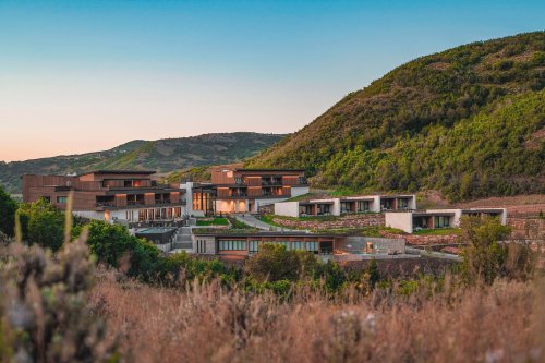 Modern hillside homes surrounded by greenery at sunset, with rolling hills in the background.