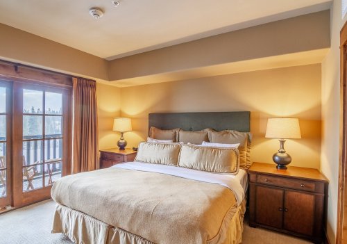 Cozy bedroom with a large bed, warm lighting, and a balcony view through wooden doors.