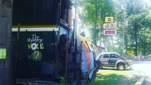 A quirky roadside attraction featuring a colorful building labeled "The Mystery Hole" and a vintage taxi parked nearby.