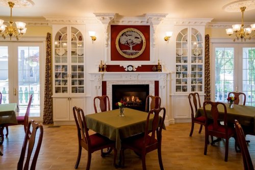 Cozy dining room with wooden tables, red chairs, a fireplace, and elegant decor featuring a tree artwork on the wall.