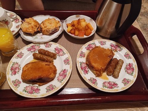 A breakfast tray with two plates of French toast, sausage links, a bowl of fruit, and a coffee pot.