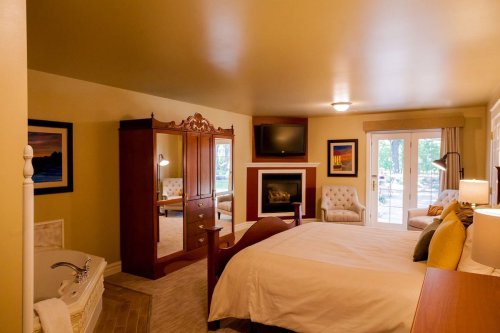 Cozy hotel room featuring a bed, fireplace, seating area, and large windows with natural light.