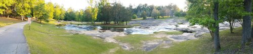 A serene landscape featuring a rocky riverbed surrounded by lush greenery and trees under a clear sky.