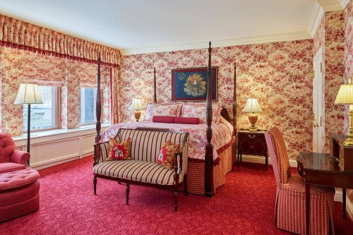 A luxurious bedroom with floral wallpaper, a four-poster bed, and elegant furnishings in warm tones.