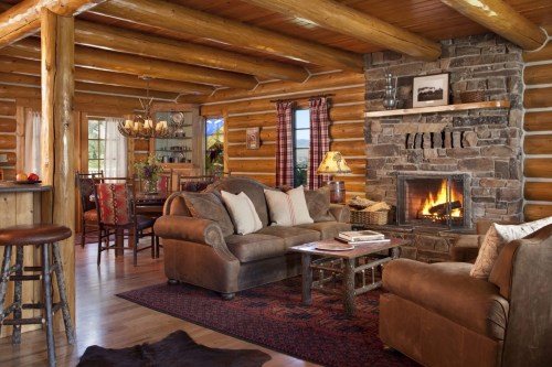 Cozy log cabin interior with a stone fireplace, comfortable seating, and rustic decor, creating a warm atmosphere.