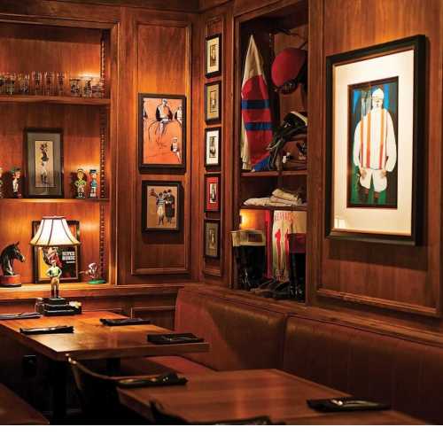 Cozy restaurant interior with wooden walls, framed art, and vintage decor, featuring a lamp and leather seating.