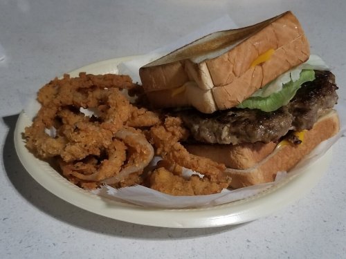 A plate with a sandwich made of two slices of bread, lettuce, cheese, and a burger patty, alongside crispy onion rings.