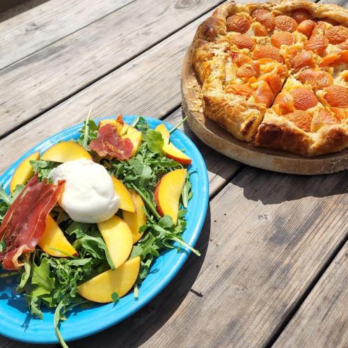 A blue plate with salad topped with peaches and prosciutto, next to a golden-brown fruit tart on a wooden table.