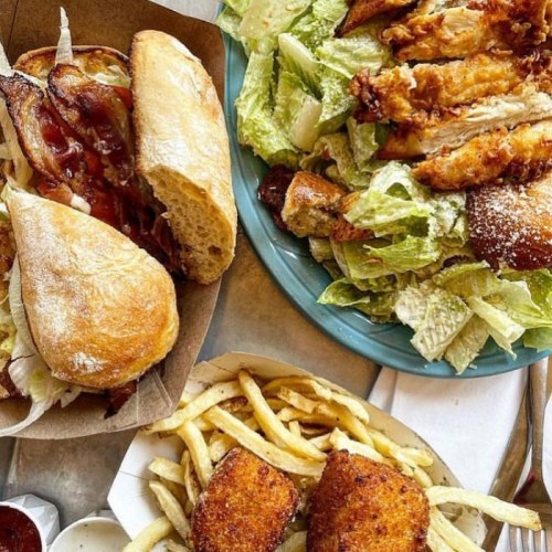 A spread of food featuring sandwiches, a Caesar salad, fries, and crispy chicken strips on a table.