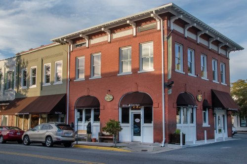 Historic brick building with a bistro and hotel, featuring large windows and awnings, on a street corner.