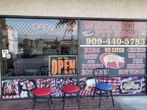 Exterior of Westside Pit BBQ with an "Open" sign, featuring a menu display and three empty chairs outside.