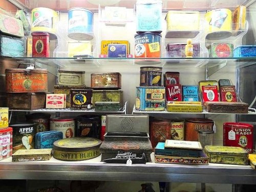 A display case filled with various vintage tin cans and boxes, showcasing colorful labels and designs.
