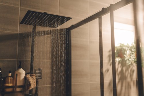 A modern shower with a rainfall showerhead, water cascading down, and a glass partition in a stylish bathroom.