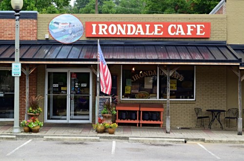 Exterior of Irondale Cafe featuring a sign, American flag, and outdoor seating with potted plants.