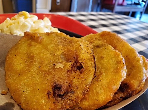 Three golden, crispy fried plantains served with a side of creamy macaroni and cheese on a checkered tablecloth.