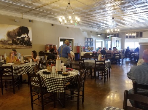 A bustling restaurant with checkered tablecloths, diners enjoying meals, and a vintage train photo on the wall.
