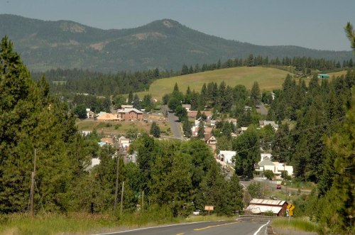 A scenic view of a small town nestled in a valley, surrounded by green hills and mountains under a clear blue sky.