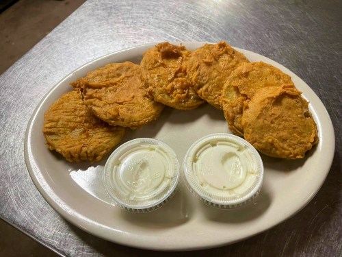 A plate of golden-brown fried patties with two small cups of dipping sauce on the side.