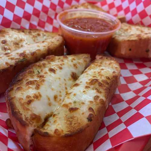 Cheesy garlic bread slices with a side of marinara sauce in a red and white checkered basket.