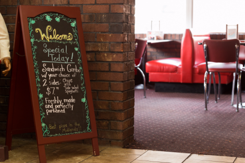 A chalkboard sign in a restaurant displays a special sandwich combo with sides for $7, welcoming customers.