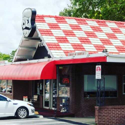 A retro-style restaurant with a red and white checkered roof and a large cartoon chef sign, featuring an "Open" sign.