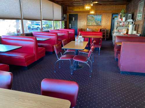 Interior of a cozy diner featuring red booths, a wooden wall, and a small table with chairs. Natural light from windows.