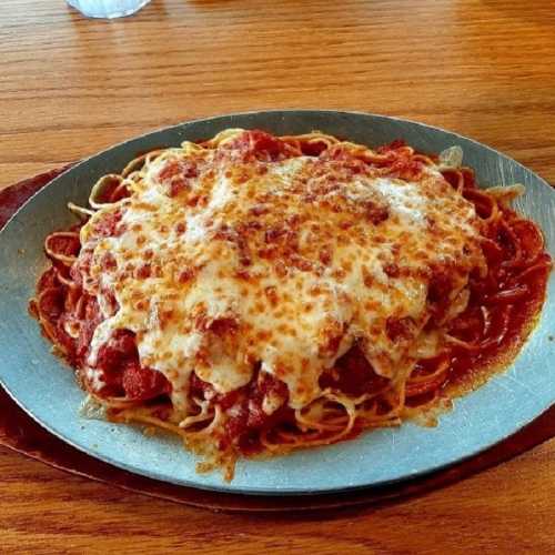 A plate of spaghetti topped with marinara sauce and melted cheese, served on a metal dish.