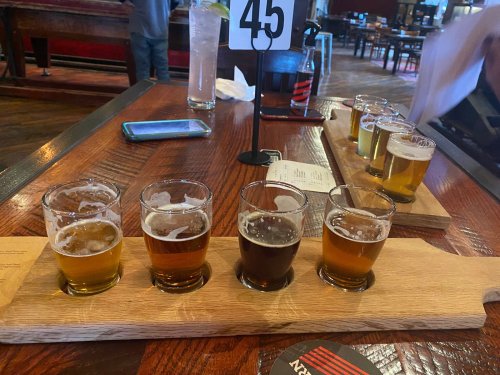 A wooden flight board with five small glasses of different beers, set on a table in a restaurant.