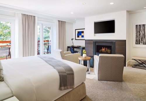 A cozy hotel room featuring a king bed, seating area, fireplace, and large windows with natural light.