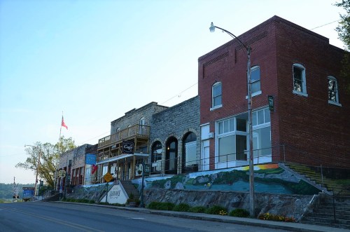 A quaint street view of historic buildings with a mural, trees, and a flag in the background.