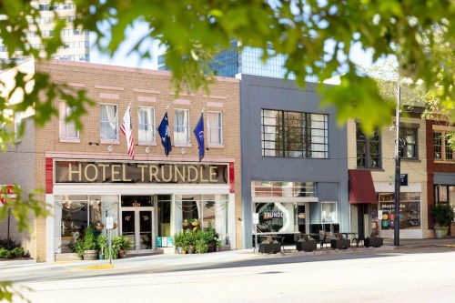 Exterior view of Hotel Trundle, featuring flags and a modern building next door, framed by green leaves.