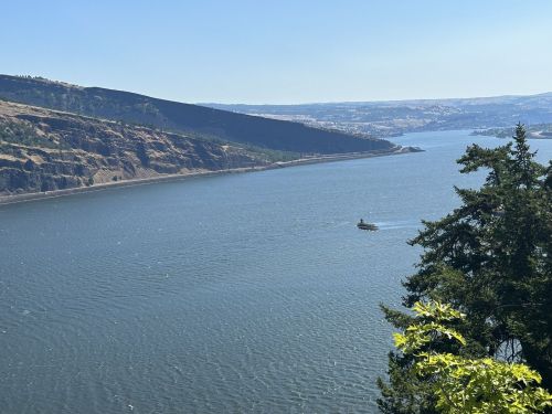 A scenic view of a river with a boat, surrounded by cliffs and lush greenery under a clear blue sky.