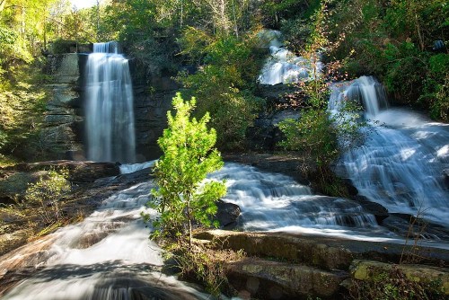 A serene waterfall cascading over rocks, surrounded by lush greenery and trees in a tranquil natural setting.