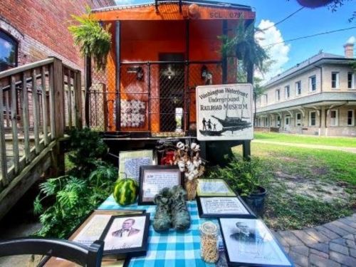 A display outside a railroad museum featuring framed photos, artifacts, and a watermelon on a checkered tablecloth.