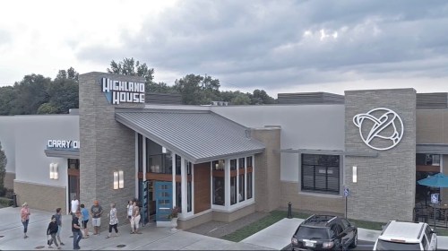 Exterior view of Highland House restaurant with a modern design, featuring a sign and people waiting outside.