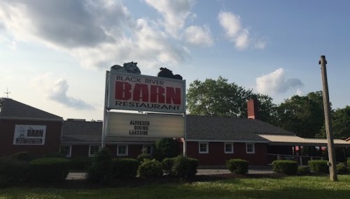 Sign for Black River Barn Restaurant, featuring "Alfresco Dining" and a view of the building surrounded by greenery.