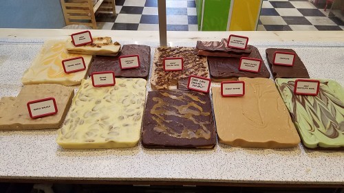 A display of various fudge flavors, including chocolate, peanut butter, and vanilla, each labeled with names.