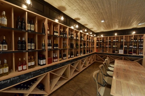 A cozy wine cellar with wooden shelves displaying various bottles of wine and a rustic wooden table.