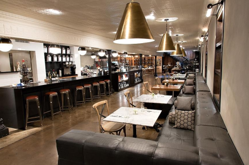 Modern restaurant interior featuring a bar, seating area, and large pendant lights. Warm, inviting atmosphere.