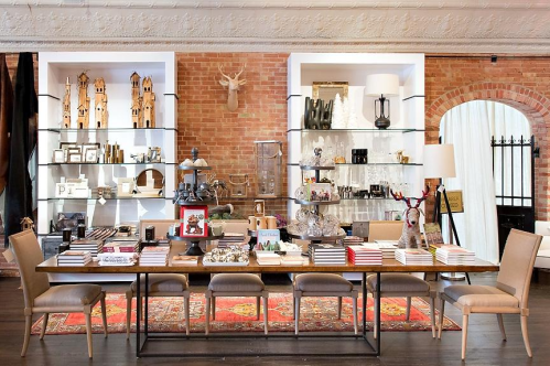 A stylish retail display featuring shelves of decor items and a table with various products in a brick-walled setting.