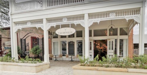 Exterior of a charming restaurant named "Vaudeville," featuring a porch, decorative details, and outdoor seating.