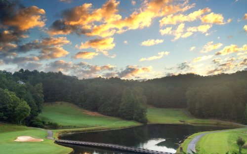 A serene golf course at sunset, featuring lush green grass, a calm pond, and colorful clouds in the sky.