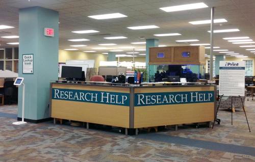 A library help desk labeled "Research Help" with computers and a kiosk in a spacious, well-lit area.