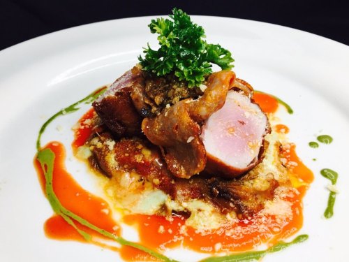 A gourmet dish featuring sliced meat atop a bed of sauce, garnished with parsley and colorful drizzles of sauce.