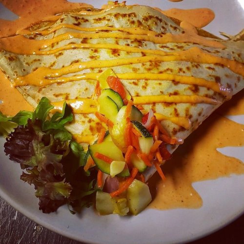 A delicious crepe drizzled with sauce, served with a side of fresh salad and colorful vegetable garnish.