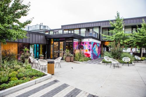 A modern building with colorful murals, surrounded by greenery and outdoor seating in a vibrant courtyard.