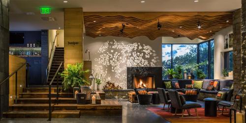 Cozy lobby with wood accents, a fireplace, plants, and a large window showcasing a scenic view. Warm, inviting atmosphere.