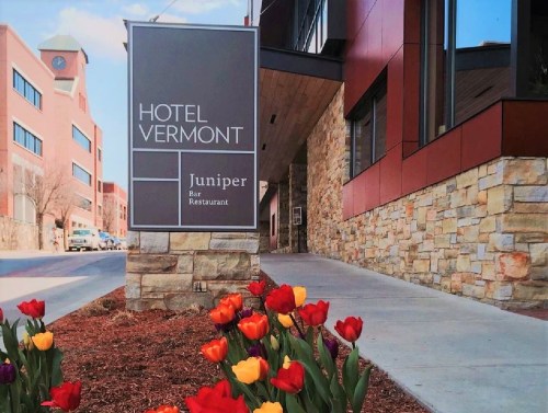Sign for Hotel Vermont with Juniper Bar Restaurant, surrounded by colorful tulips and a modern building facade.
