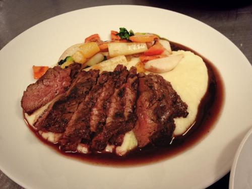 A plate of sliced beef served with mashed potatoes and colorful sautéed vegetables, drizzled with a rich sauce.