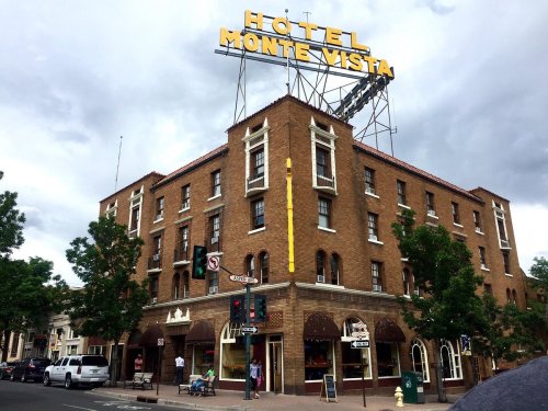 Historic Hotel Monte Vista building with a large sign, surrounded by trees and street activity under a cloudy sky.